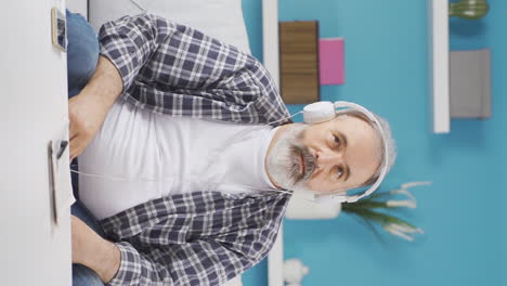 Vertical-video-of-Old-man-listening-to-music-with-headphones-is-unhappy-and-sad.